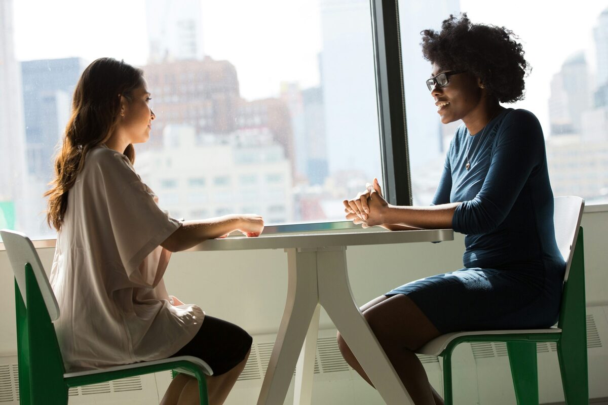 Two people in conversation beside a sunlit window.