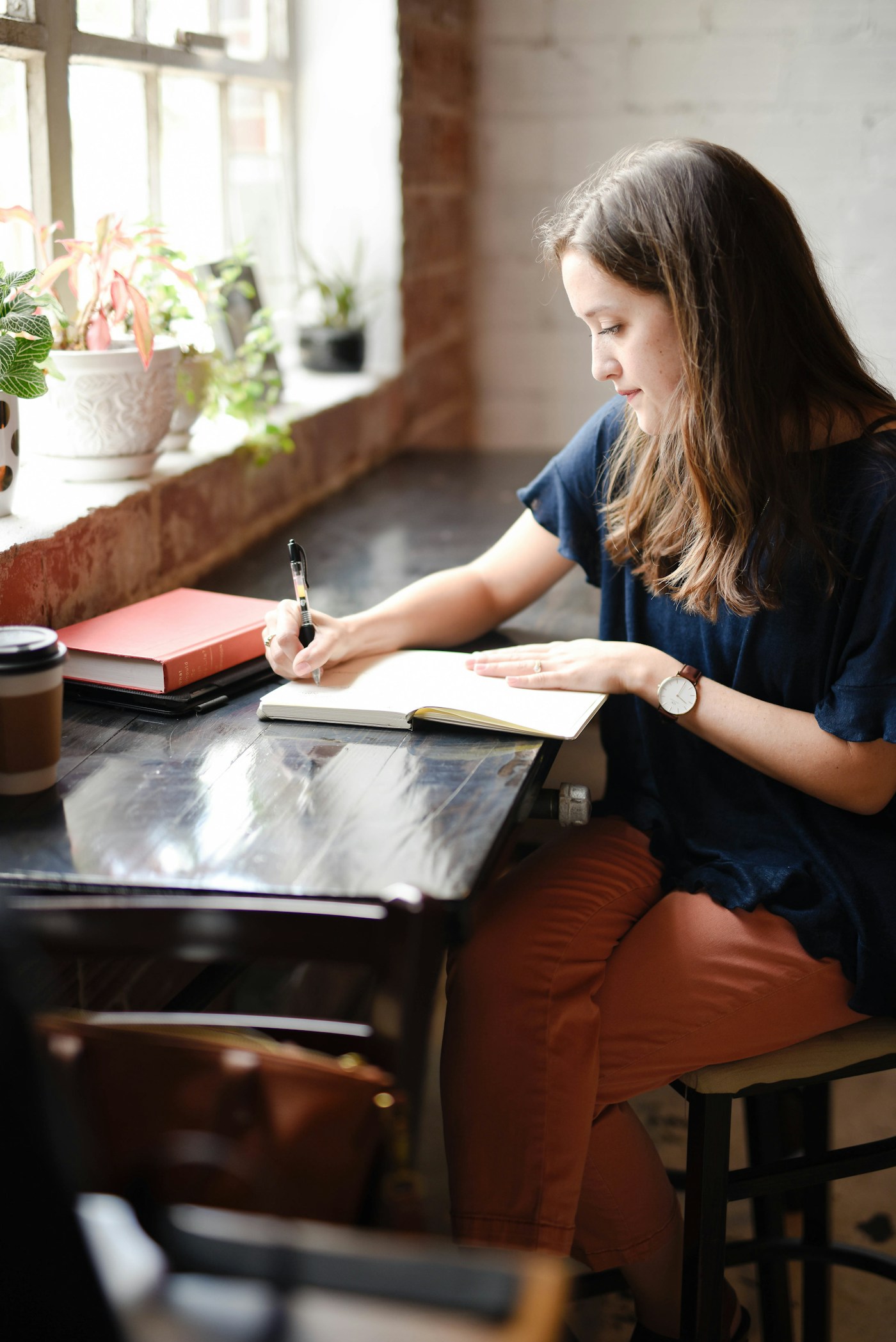 A woman writing in an open notebook beside a sunlit window.